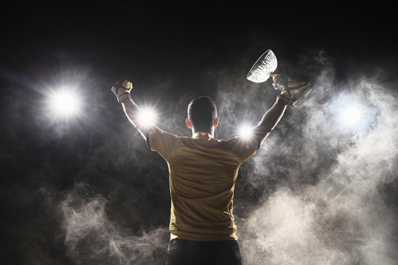 Successful Soccer player holding crystal cup and celebrating victory on smoky background