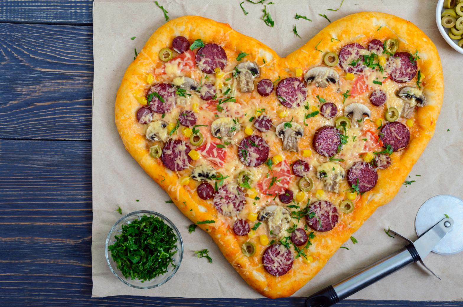 Tasty pizza in a heart shape with mushrooms, salami, pepperoni, olives, corn . The top view