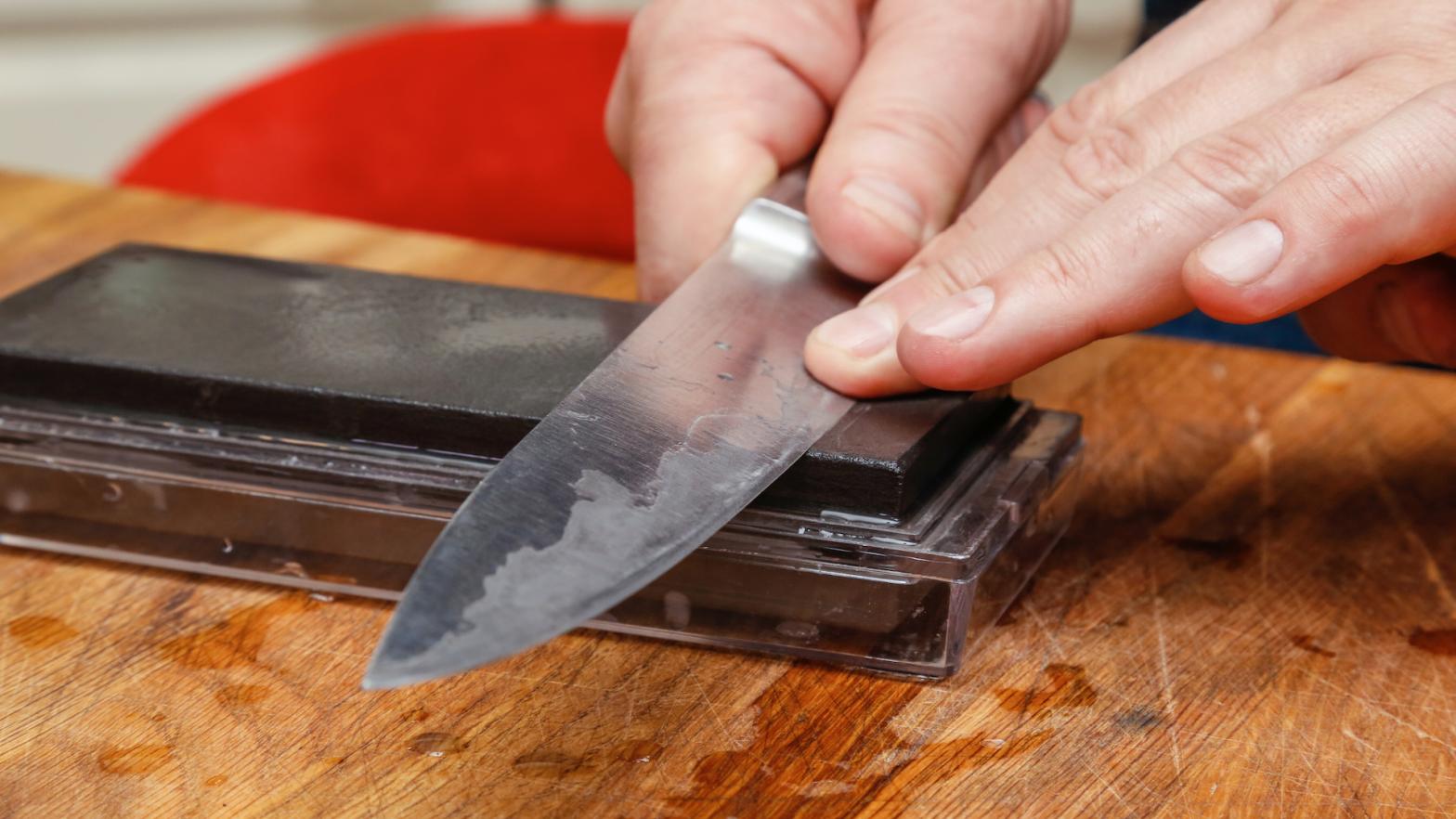 Sharpening knife on sharpening stone. Close up of man using whetstone for sharpening knife blade.