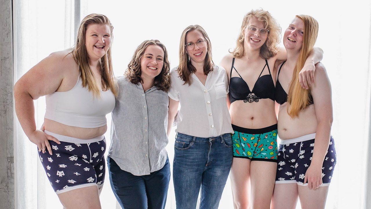 Five people with their arms around each other, three of them are wearing comfy undies for FAB people, while two fully dressed people stand in the middle