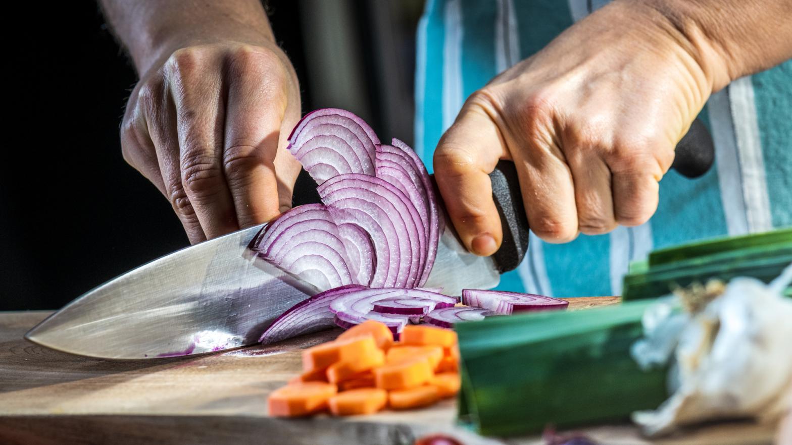 Man cutting vegetable in kitchen. Male hands making thin slices of purple onion.