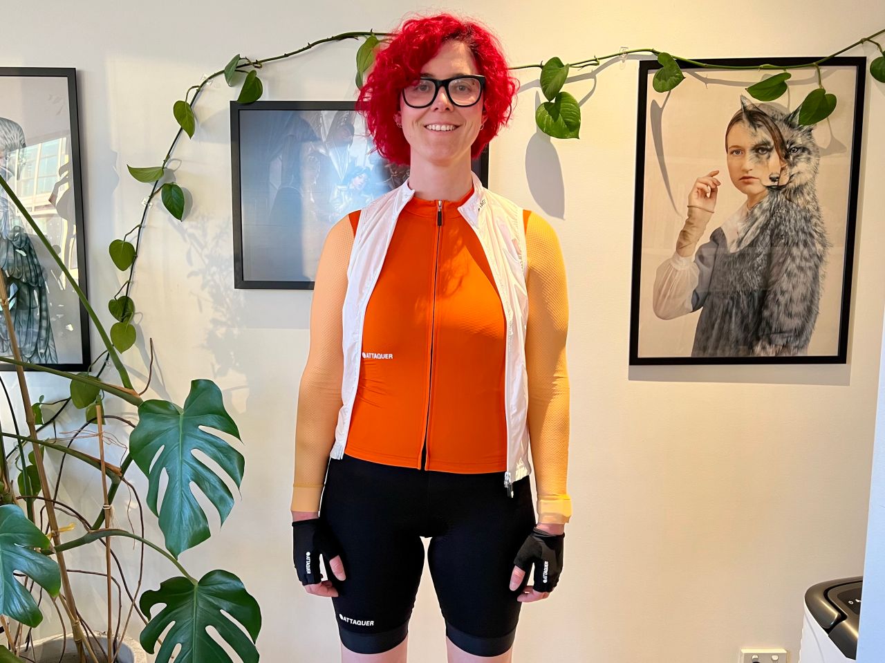 A person wearing a women's cycling kit from Attaquer. Black shorts, bright orange top, white vest